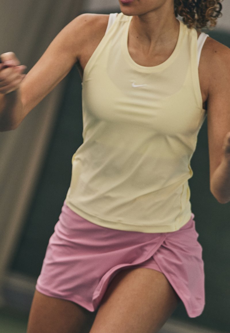 Nike Sport-Top in Hellgelb, kombiniert mit einem rosa Sportrock. Das Top hat dünne Träger, und der Rock hat ein Wickeldesign.