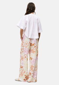 Weißes Leinenshirt mit kurzen Ärmeln und gefaltetem Rücken, kombiniert mit weiten, floralen Hosen in Rosa-, Orange- und Gelbtönen, die eine leichte Textur aufweisen.
