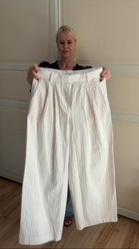 Woman holding wide-leg white pants with thin vertical stripes in front of beige closet doors.