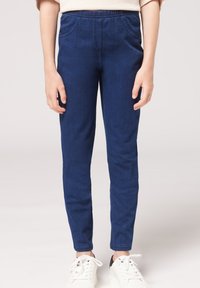 Modré strečové džíny s elastickým pasem, slim fit designem a bočními kapsami. Spárováno s bílými teniskami pro kontrast.