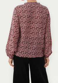 Fließende schwarze Bluse mit pinkfarbenem Blumenmuster, langen Ärmeln mit elastischen Bündchen, hohem Kragen und halbtransparenter Textur.