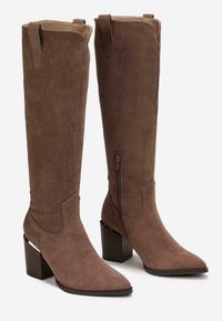 Bottes marron en daim jusqu'au genou avec des bouts pointus, des talons bloc, des fermetures éclair latérales et des tirettes en haut. Texture lisse et détails cousus.