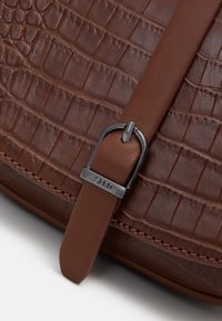 Brun läderväska med krokodiltextur som har en slät läderrem och ett metallspänne graverat med "ESPRIT."