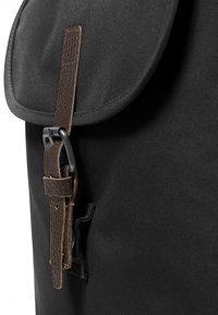 Black fabric backpack with a rounded flap, featuring a dark brown leather strap and metal buckle for closure. Textured fabric surface.