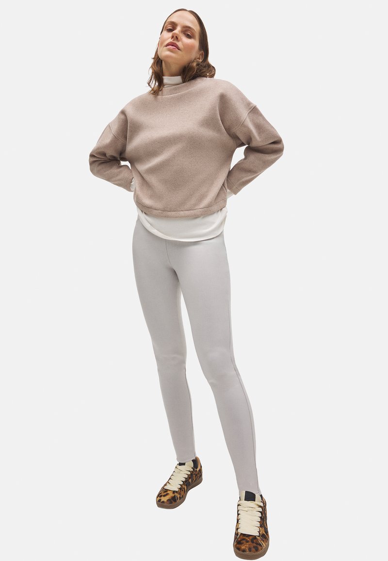 Sudadera de forro polar rosa, camiseta blanca bajo capa, leggings gris claro y zapatillas de leopardo. Corte holgado, textura suave y colores contrastantes.