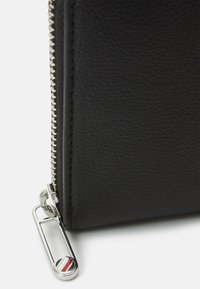 Black leather wallet with a textured finish, featuring a silver zipper and a hardware accent with red and blue details.