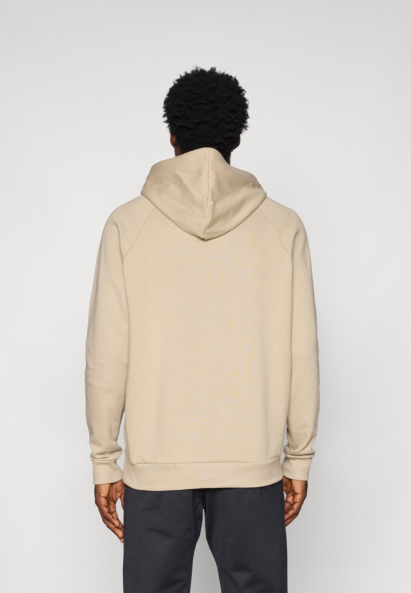 Hoodie beige con cappuccio, polsini e orlo a costine, dalla texture liscia e dal taglio rilassato, abbinato a pantaloni scuri.