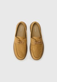 Tan slip-on shoes with a textured leather upper, contrasting brown rubber sole, and decorative lacing detail on the vamp.