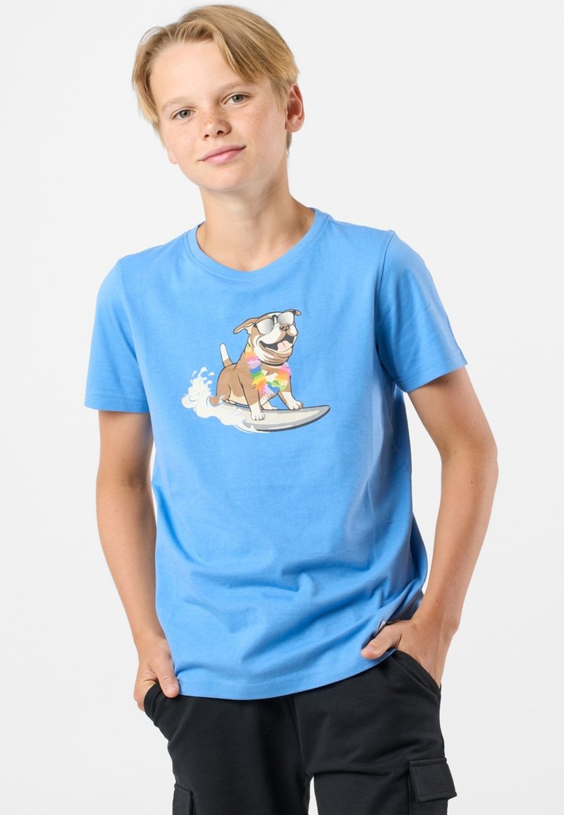 Ljusblå bomullströja med kort ärm som har en tecknad hund på en surfbräda, med solglasögon och en regnbågsfärgad krage, samt rundad hals.