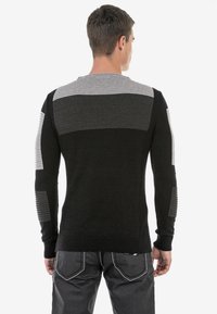 Schwarzer und grauer gestrickter Pullover mit einem strukturierten Design und horizontalen Streifen. Schlanker Schnitt, lange Ärmel und gerippte Bündchen.