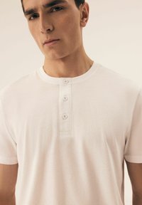 White short-sleeve henley shirt made of soft cotton, featuring three front buttons and a round neckline, with a smooth, lightweight texture.