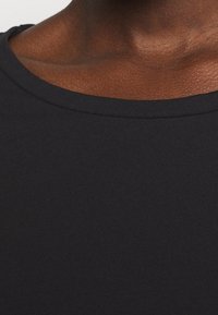 Svart bomulls t-shirt med rund halsringning och ribbad textur, som visar släta ytor utan synliga mönster eller designer.