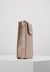 Szczupła, prostokątna torba w kolorze metalicznego różowego złota, z fakturowaną powierzchnią, złotymi okuciami oraz bezpiecznym zamknięciem od góry z boczną klapką.
