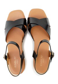 Zwarte leren sandalen met een design van kruislings banden, vlakke zool en verstelbaar enkelbandje. Bruine binnenzool met gouden branding. Glad oppervlak.