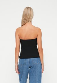 Schwarzes, trägerloses Top mit einem enganliegenden Oberteil, maßgeschneiderten Nähten und einer glatten Textur. Kombiniert mit hochtaillierten, hellblauen Jeans.