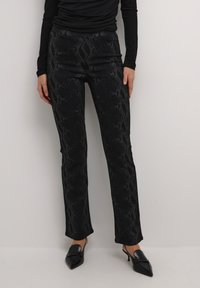 Zwarte slangenprint broek met een getailleerd silhouet, textuurstof en een lichte flared onderkant, gecombineerd metpuntige zwarte hakken.