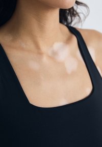 Prenda negra ajustada con escote cuadrado, que muestra una textura de tejido suave y piel visible con manchas más claras debajo.