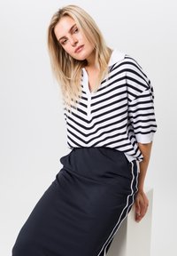 Gestreepte polo in zwart en wit met een chevronpatroon, gecombineerd met een effen zwarte rok met witte zijstrepen.