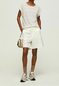 Gestreepte beige top, witte shorts, beige sneakers met accenten. Accessoires omvatten een geweven tas met zwart-witte details.