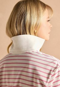 Svītrainā polo krekls ar baltām un gaiši rozā horizontālām svītrām, izceļoties ar augstu baltu apkakli un mīkstu kokvilnas audumu.