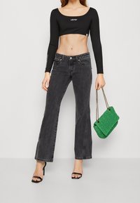 Top negro de manga larga recortado con el logo "LEVI'S", combinado con pantalones de mezclilla negros de tiro alto y campana, y un bolso verde texturizado.