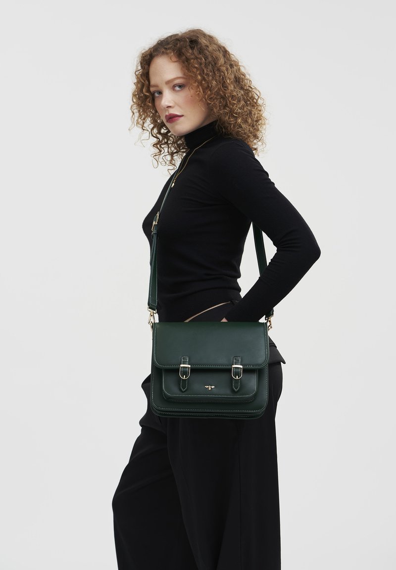 Borsa a spalla verde in pelle con due fibbie frontali, design piatto e tracolla rimovibile. Texture liscia e dettagli in metallo dorato.