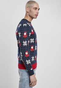 Pull de Noël en tricot avec une base bleu marine, des motifs de Père Noël rouges et des flocons de neige blancs, ourlet et poignets côtelés de couleur rouge contrastante.