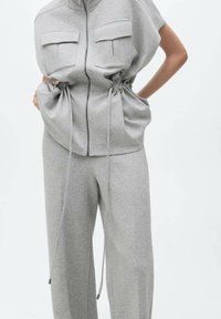 Completo grigio a due pezzi composto da una maglietta con maniche corte e zip, dotata di due tasche frontali e vita con cordino, abbinata a pantaloni larghi coordinati.