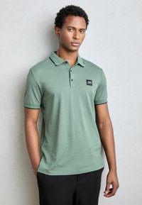 Groene polo shirt van katoen, met een kraag, korte mouwen en een vierkante logo-patch op de linkerborst. Glad oppervlak.