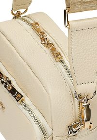 Borsa a tracolla in pelle crema con doppie zip dorate, tracolla regolabile e superficie texturizzata. Le finiture dorate accentuano il design.