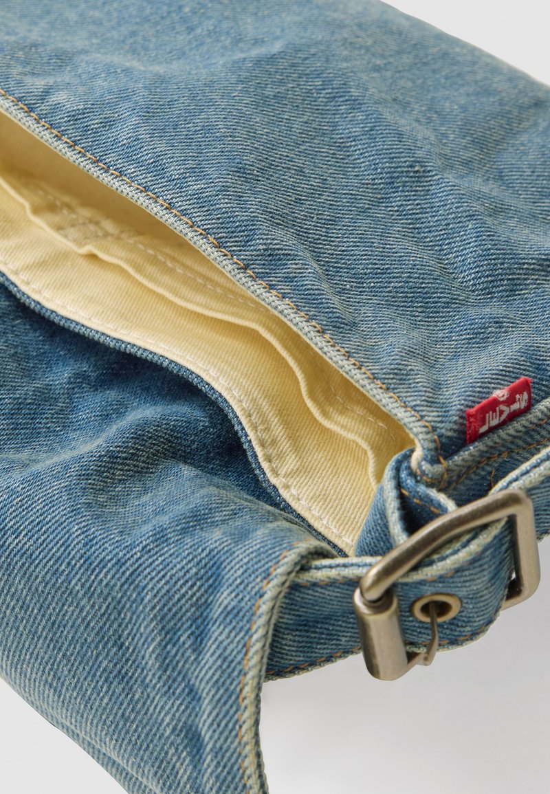 Borsa in denim blu con rivestimento in tessuto beige, fibbia in metallo e piccolo etichetta rossa sul lato.