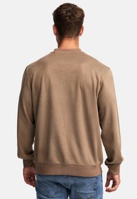 Bruine sweatshirt met een gladde textuur, geribbelde manchetten en kraag, met een eenvoudig ontwerp. Draagt met blauwe spijkerbroek.