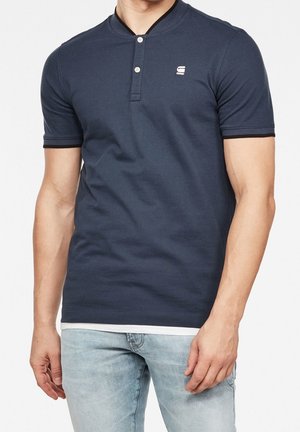 Polo bleu marine en coton, avec un col boutonné, des manches courtes à bordure contrastante, et un petit logo sur la poitrine.