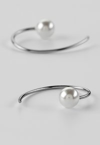 Silberne Creolen mit glatten weißen Perlen. Das Design weist eine geschwungene Form auf, die die glänzende, reflektierende Oberfläche der Perlen deutlich zur Geltung bringt.