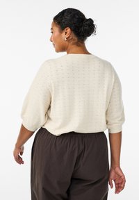 Suéter color crema hecho de tela de punto texturizada, con un ajuste holgado, mangas abullonadas y escote redondeado, combinado con pantalones oscuros.