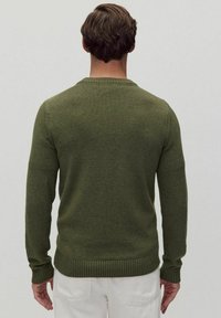 Grön stickad tröja med rundad halsringning, ribbstickade ärmslut och nederkant, som visar en slät struktur och figurnära design.