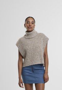 Pull en tricot beige chunky avec un col roulé haut et replié, à manches courtes, associé à une jupe en denim bleue. Tissu texturé avec des éclats.