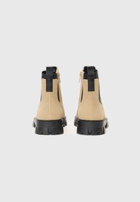 Botines de ante beige con acentos de cuero negro, con cremallera y suela de goma negra texturizada. Punta redondeada y diseño robusto.