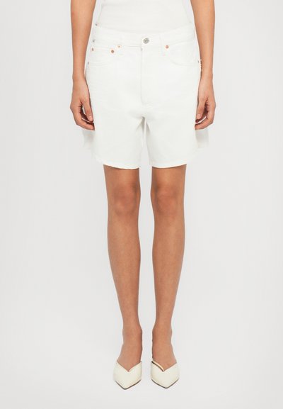 Shorts in denim bianco con taglio dritto, dotati di chiusura con bottone, tasche frontali e orli sfrangiati. Indossati con tacchi bianchi a punta.