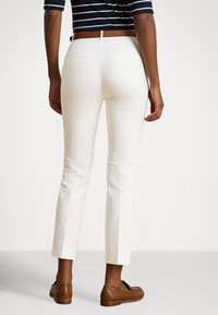 Λευκό στενό παντελόνι με πίσω τσέπες, λεπτομέρειες ραφών και καφέ δερμάτινη ζώνη. Συνδυάζεται με καφέ μοκασίνια. Φορά μπλούζα με ρίγες.