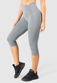 Jasnoszare legginsy z wysokim stanem, wykonane z gładkiego, elastycznego materiału, z płaskimi szwami i długości capri, w połączeniu z czarnymi butami sportowymi.