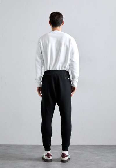 White crew-neck sweatshirt, black tapered pants with elastic waistband, and patterned sneakers. Minimalist design, smooth texture, rear view.