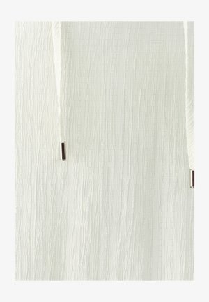 Close-up of white textured fabric with vertical ridges and two white drawstrings ending in silver metal tips.