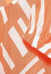 Orange fabric featuring a bold white zigzag pattern, with a gathered sleeve detail. Texture appears lightweight and smooth.