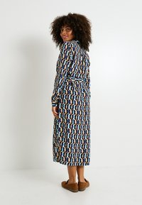 Vestido largo y estampado con formas geométricas en tonos beige, azul y marino. Confeccionado en tela suave, tiene mangas largas y una cintura ceñida con cinturón.