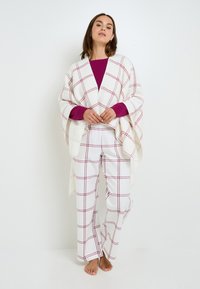 Poncho bianco a quadri con linee rosse, abbinato a pantaloni bianchi con motivo a quadri coordinato. Tessuto morbido, vestibilità comoda, stile casual.