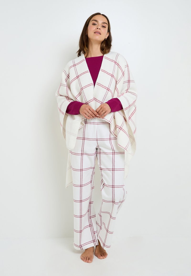 Poncho bianco a quadri con linee rosse, abbinato a pantaloni bianchi con motivo a quadri coordinato. Tessuto morbido, vestibilità comoda, stile casual.