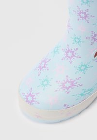 Primer plano de una bota de lluvia azul claro con patrones de copos de nieve morados, rosas y azul turquesa y una suela blanca sobre un fondo blanco.