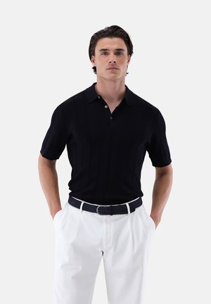 Polo shirt nero lavorato a maglia con colletto e maniche corte, abbinato a pantaloni bianchi e una cintura nera intrecciata. Design semplice e strutturato.