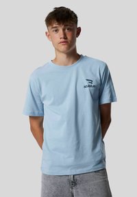 T-shirt en coton bleu clair avec des manches courtes et un col rond, arborant un petit logo "sculpture" bleu foncé sur la partie gauche de la poitrine.